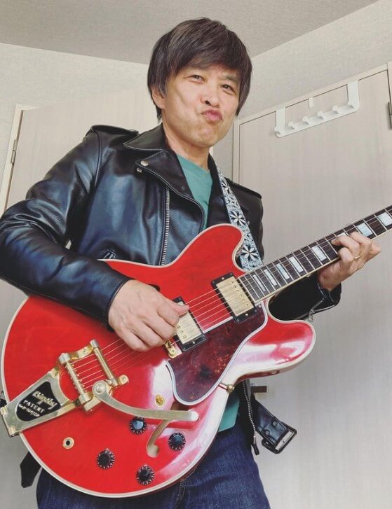 武田真一アナウンサーが佐野元春のようにギターを片手にポーズを決めている画像